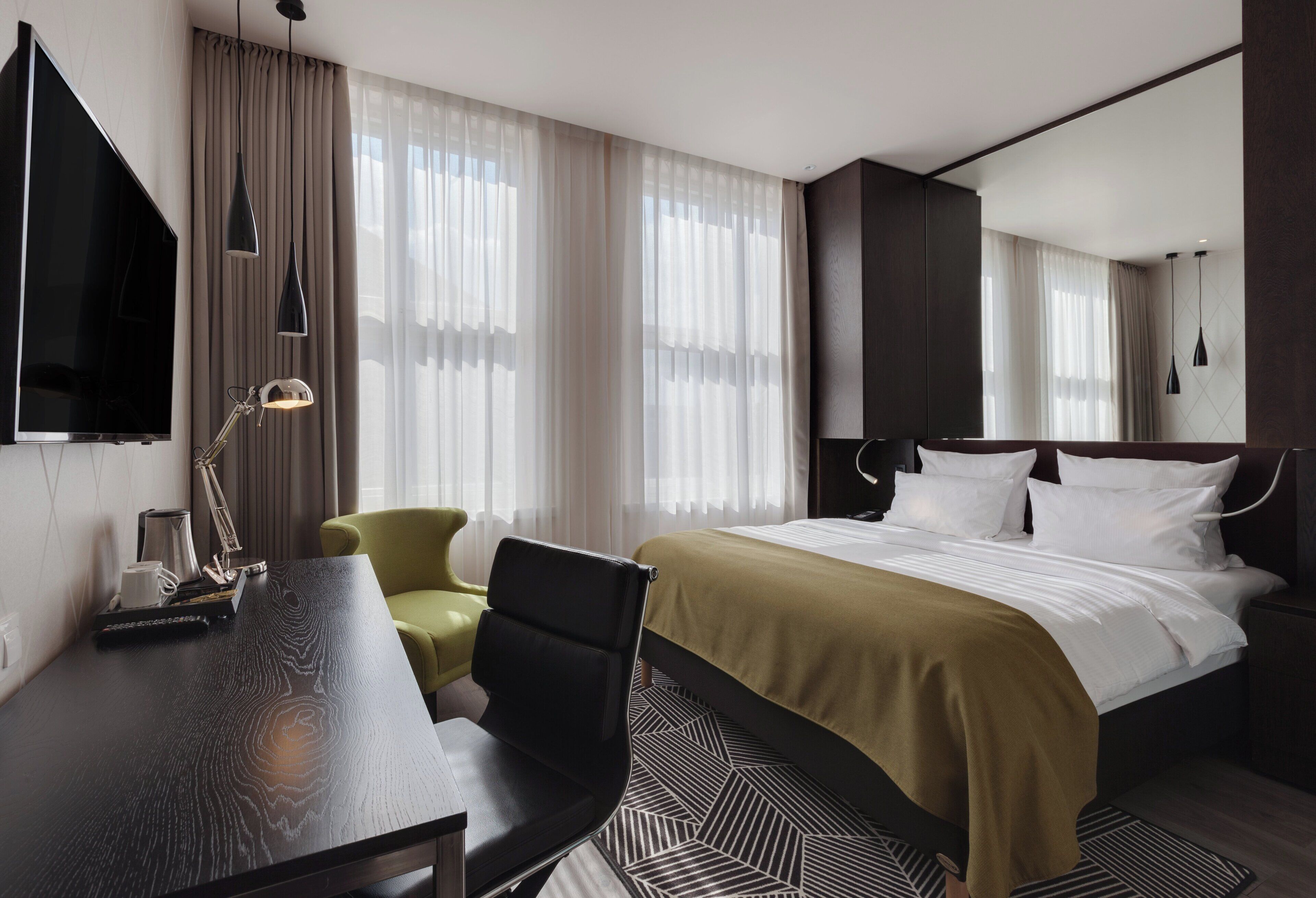 Habitación de hotel con cama, escritorio, silla, televisión y ventana con cortinas.