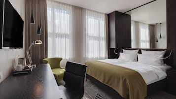 Habitación de hotel con cama, escritorio, silla, televisión y ventana con cortinas.