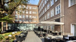 An outdoor cafe area with tables and chairs, surrounded by potted plants and a large tree. - Holiday Inn Dresden - Am Zwinger by IHG (Dresden)