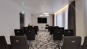 A conference room with a patterned carpet, rows of chairs, a table, and a flat-screen TV mounted on the wall.