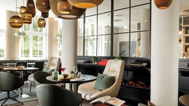 A modern lounge area with leather seating, a fireplace, and large windows offering natural light. - Holiday Inn Dresden - Am Zwinger by IHG (Dresden)