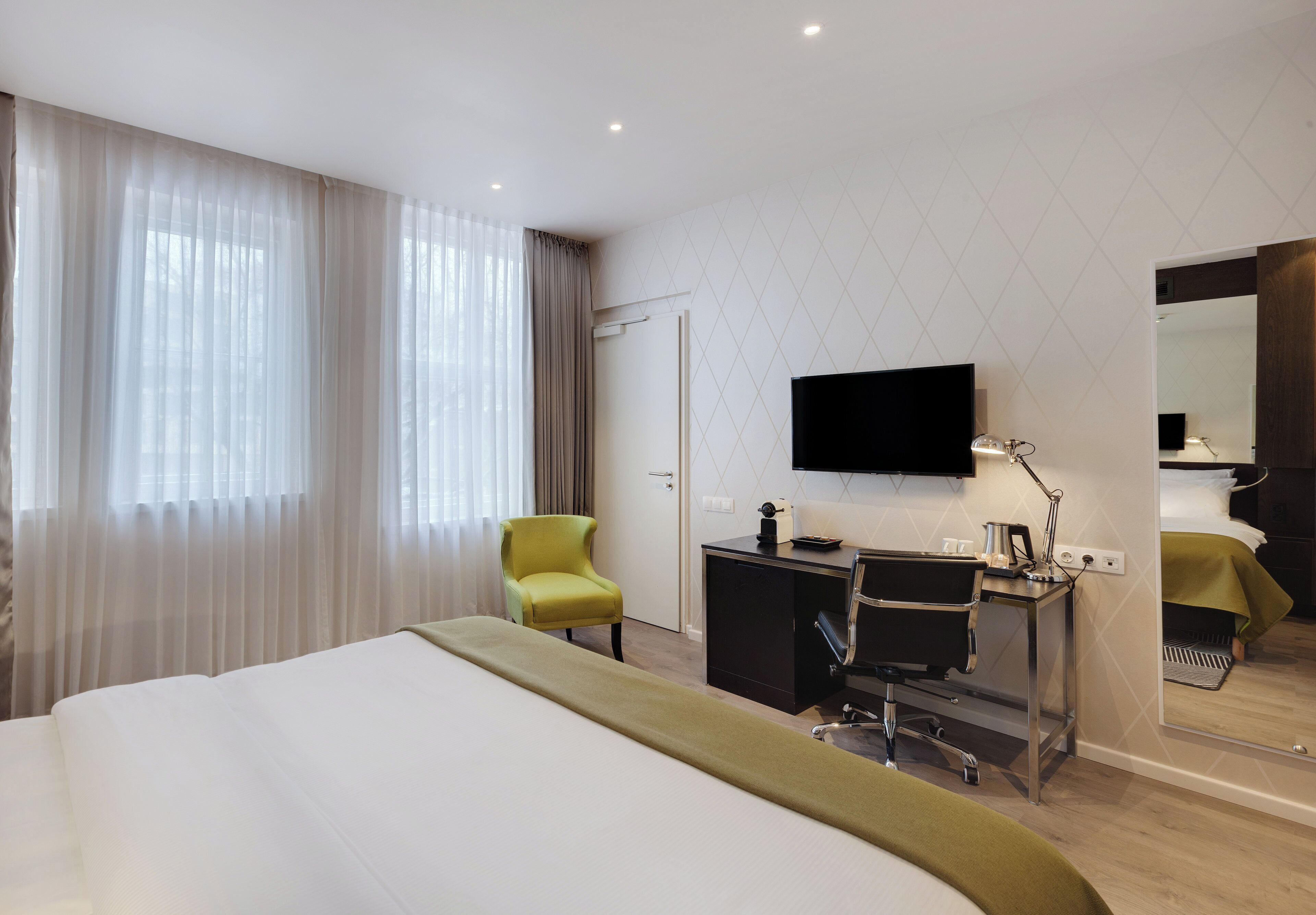 Ein Hotelzimmer mit Bett, Schreibtisch, Stuhl, Fernseher und Spiegel.