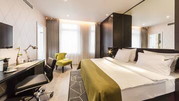 Ein modernes Hotelzimmer mit einem großen Bett, einem Schreibtisch mit Computer, einem Sessel und einem großen Fenster mit Vorhängen.