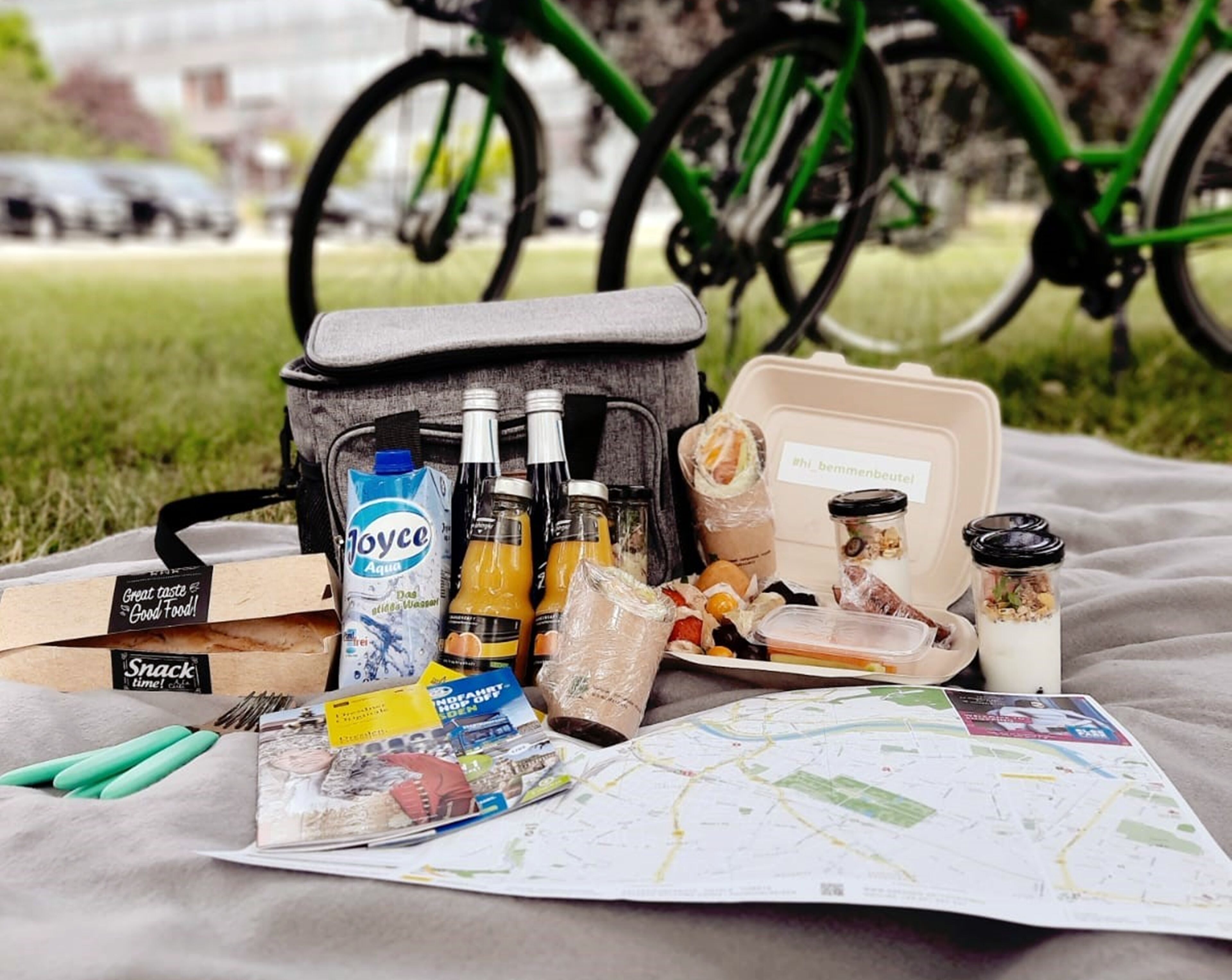 A picnic setup with a bag containing snacks, drinks, and a map on a blanket.