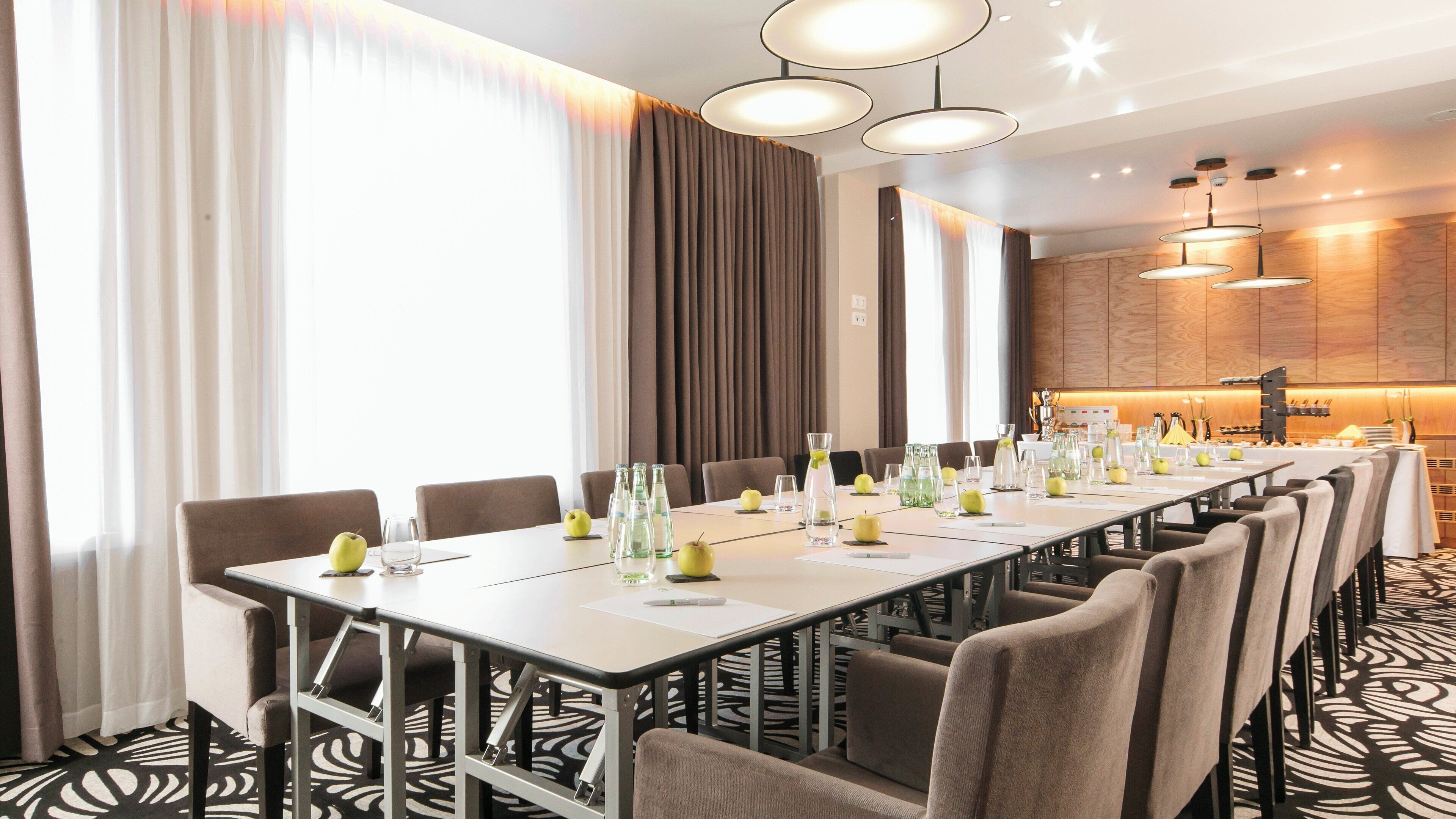 A conference room with a long table, chairs, and a kitchen area in the background.