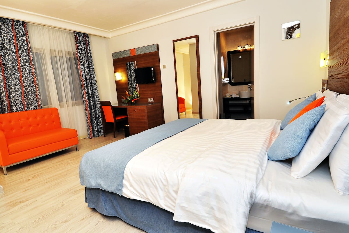 A hotel room with a large bed, a bright orange sofa, a desk, and a mirror.
