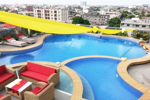 A rooftop swimming pool with lounge chairs and a table, surrounded by a cityscape view. - Bénin Royal Hôtel (Cotonou)