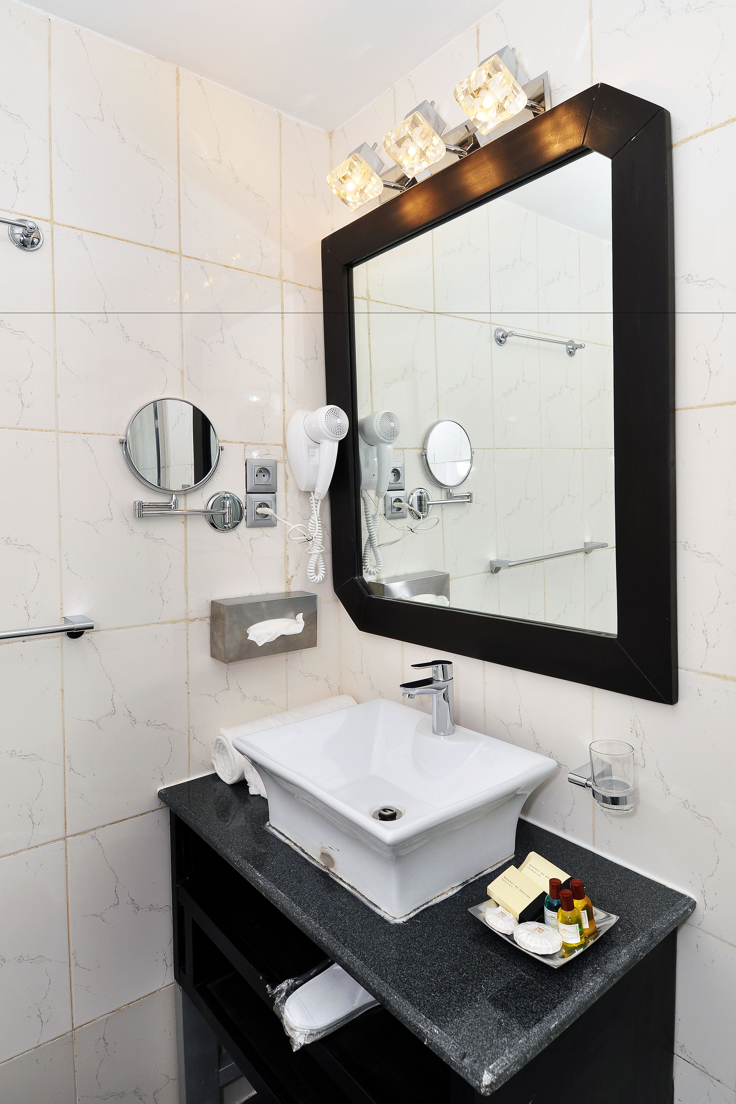 Ein Badezimmer mit weißem Waschbecken, schwarzer Arbeitsplatte und einem großen Spiegel mit Beleuchtung.