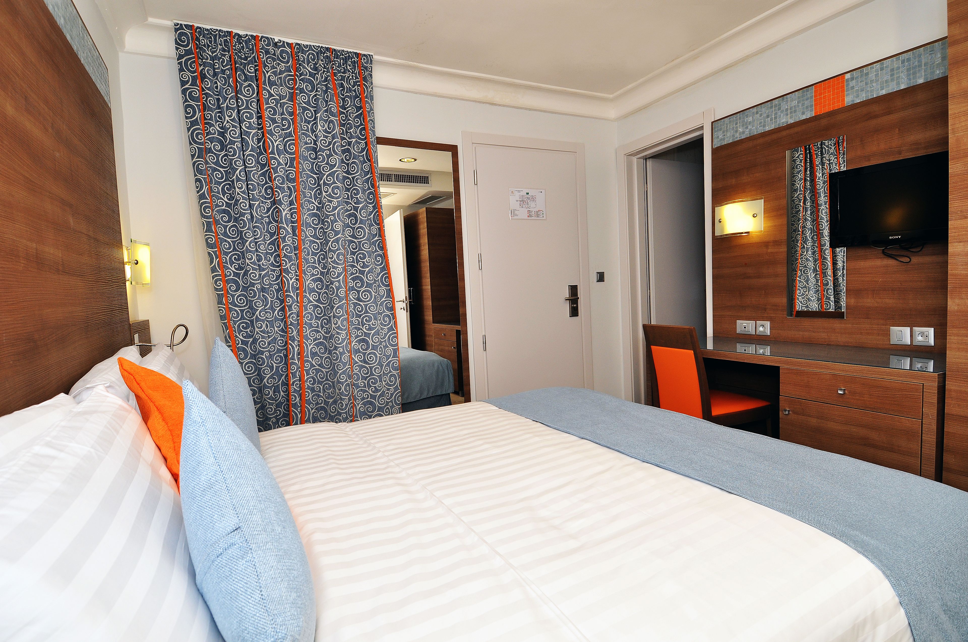 Habitación de hotel con una cama grande, un escritorio, una silla, un televisor y un armario.