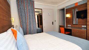 Habitación de hotel con una cama grande, un escritorio, una silla, un televisor y un armario.