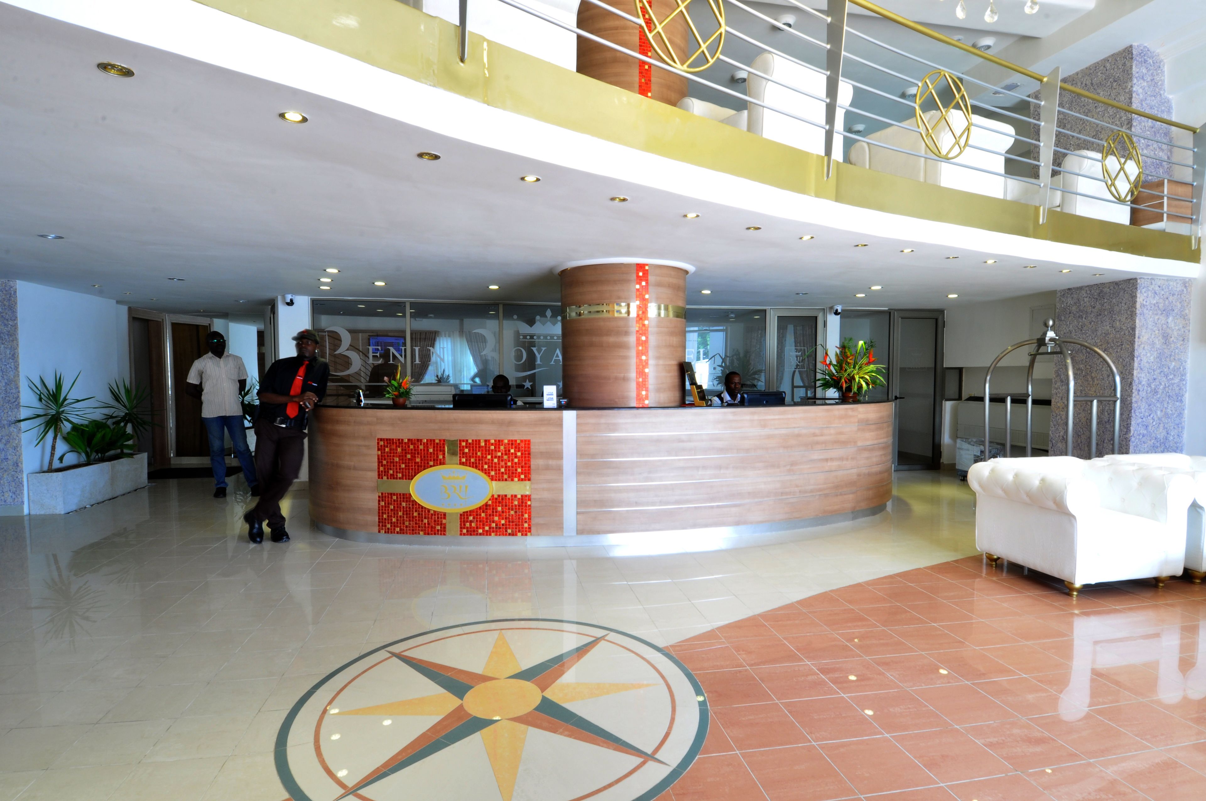 A hotel reception area with a modern design, featuring a central desk, a staircase, and a lounge area with a white sofa.