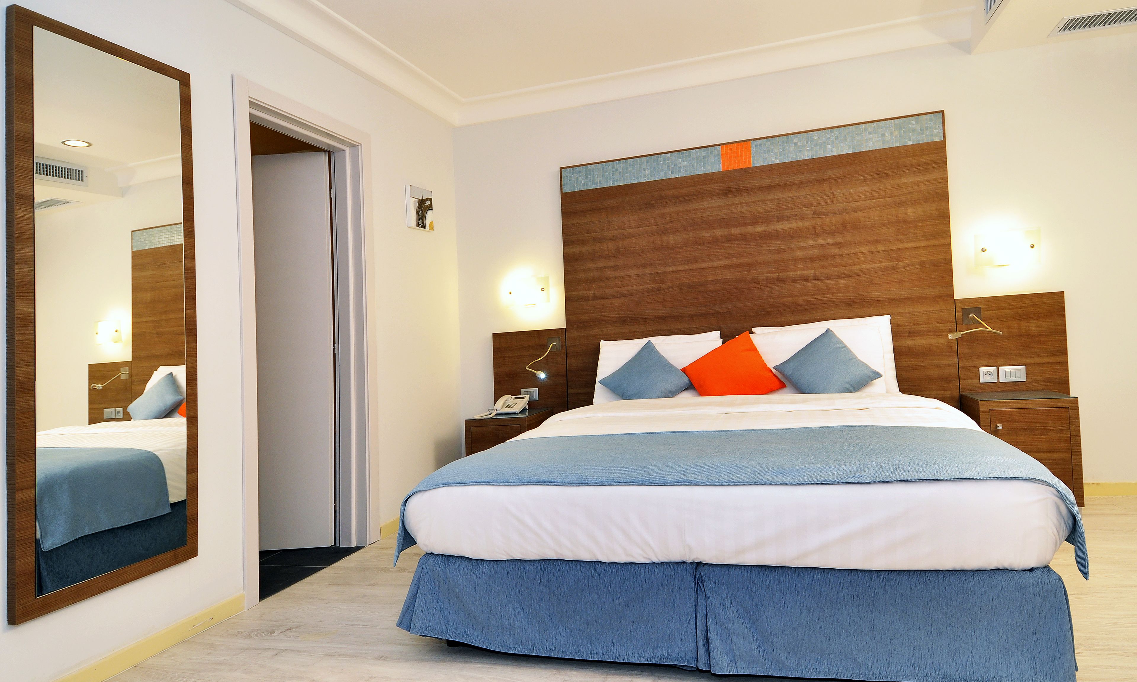 Una camera d'albergo con un letto grande, un comodino, uno specchio e una porta.