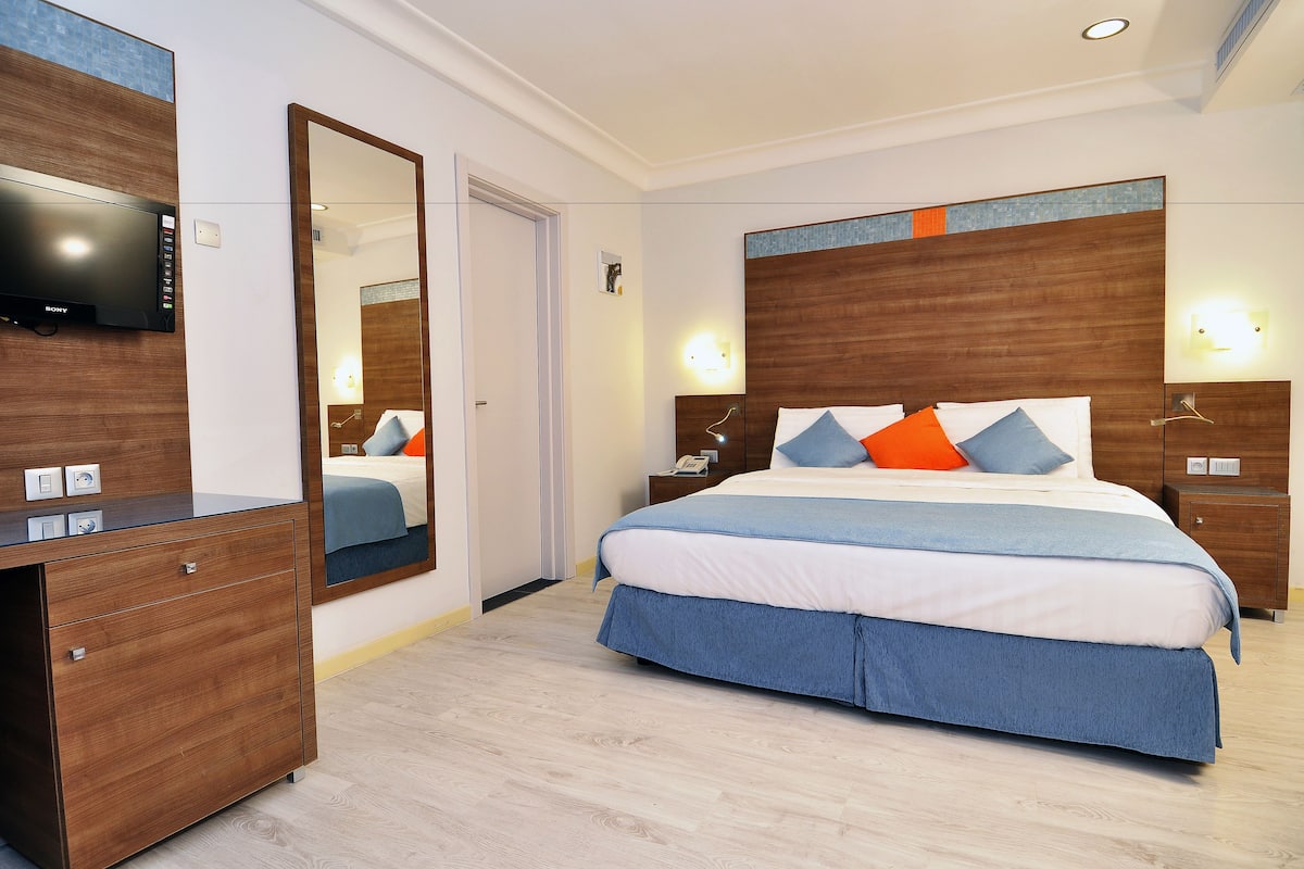 A hotel room with a large bed, a wooden dresser, a flat-screen TV, and a mirror.