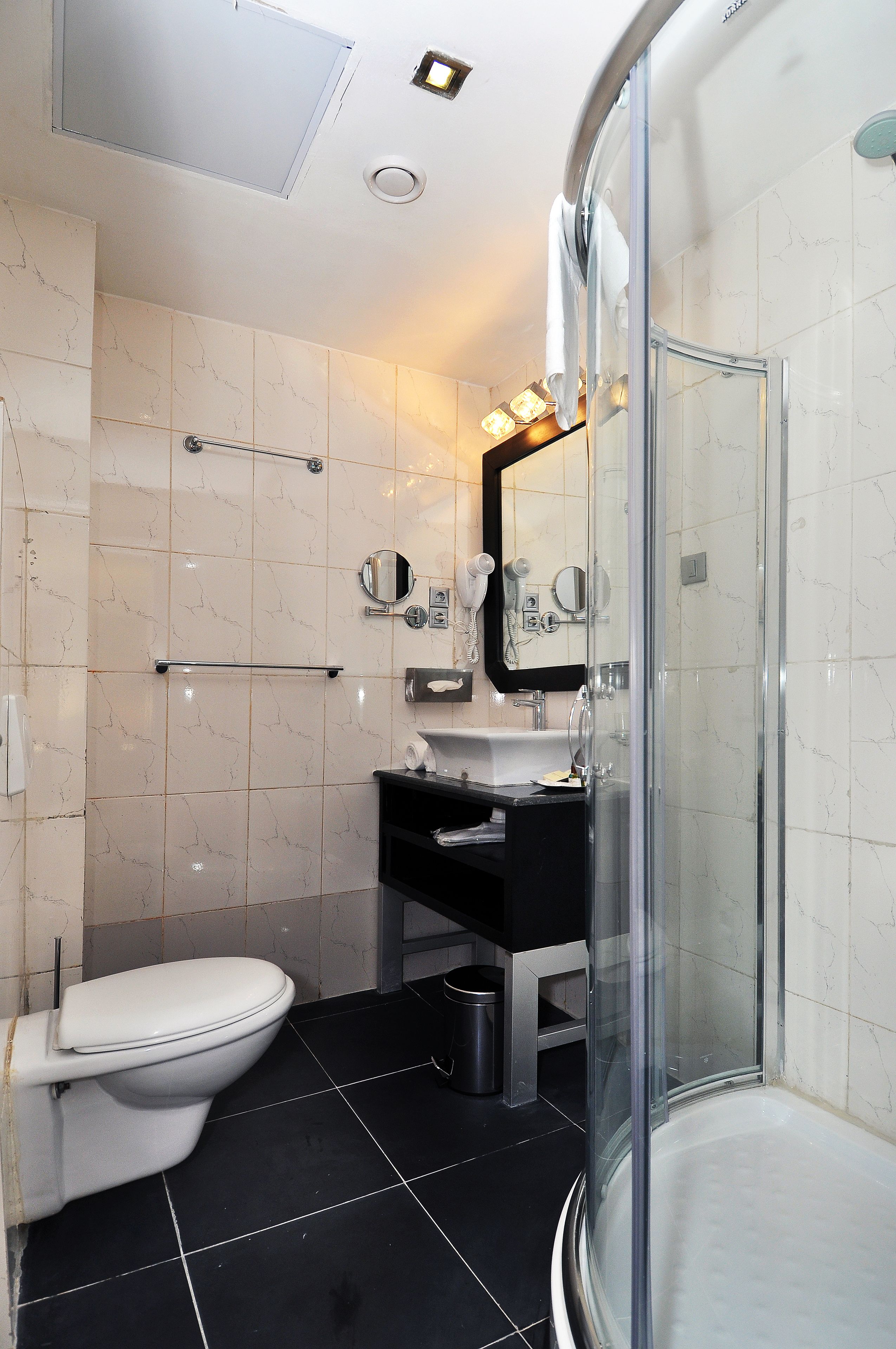 Un baño moderno con cabina de ducha de vidrio, inodoro blanco y lavamanos negro.