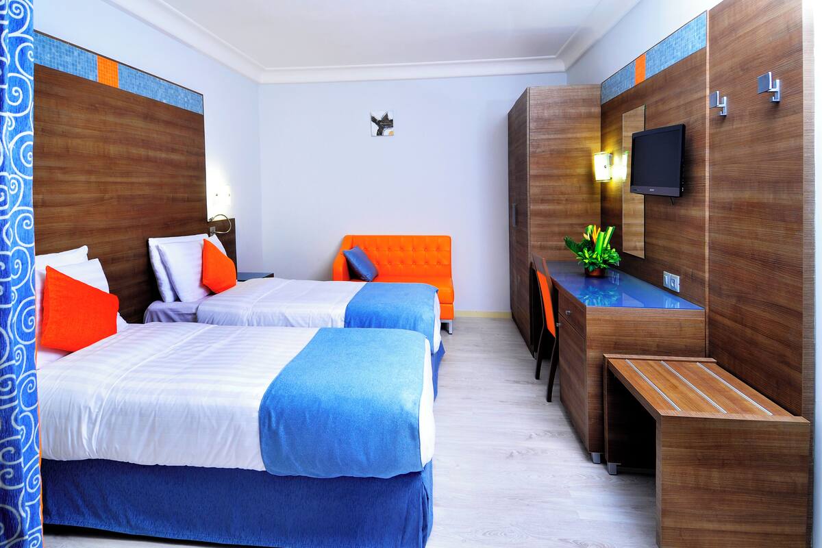 A hotel room with two beds, a desk, a mirror, and a television.