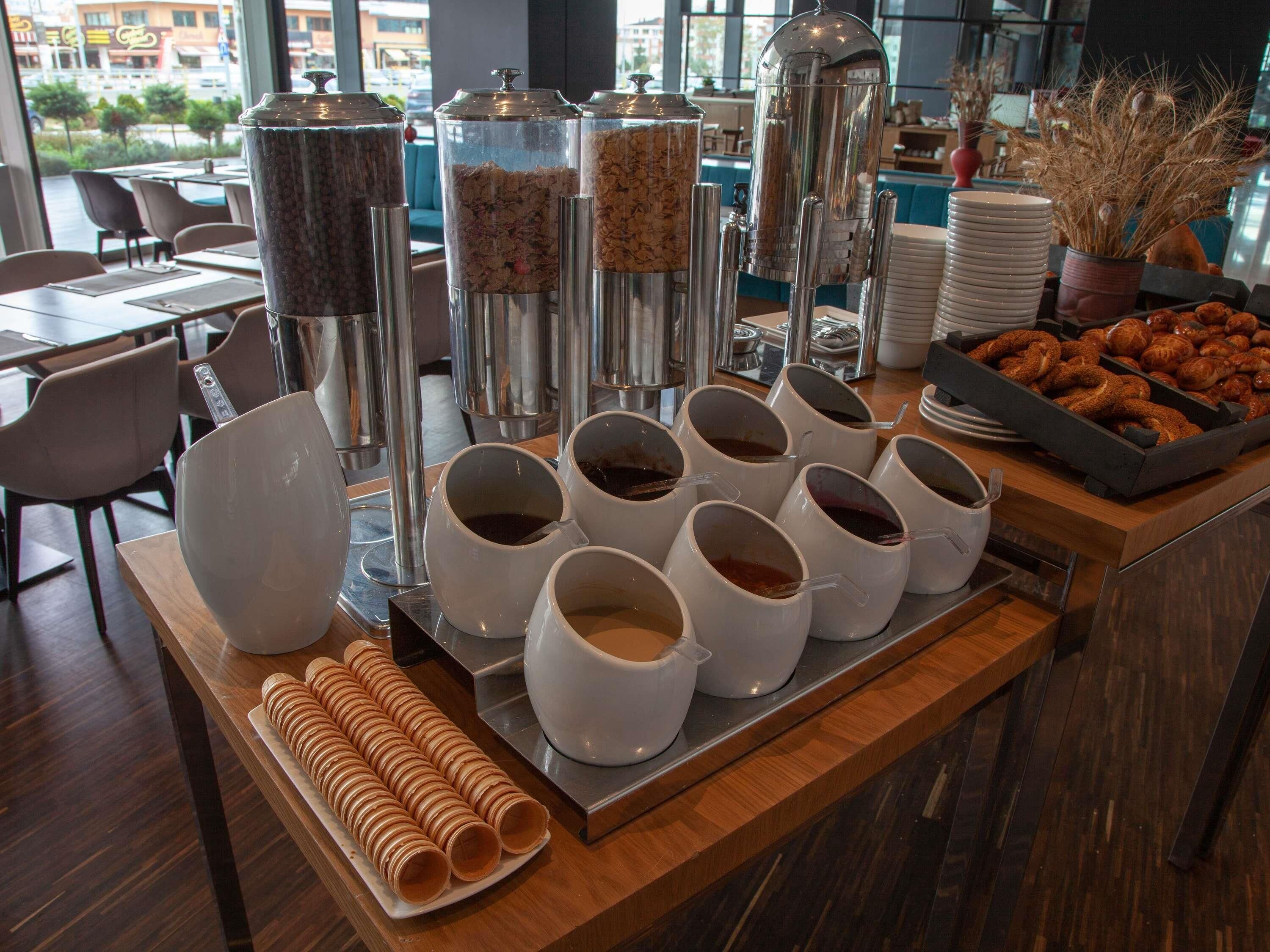 Un buffet de petit-déjeuner avec des urnes à café, des distributeurs de céréales et des viennoiseries.