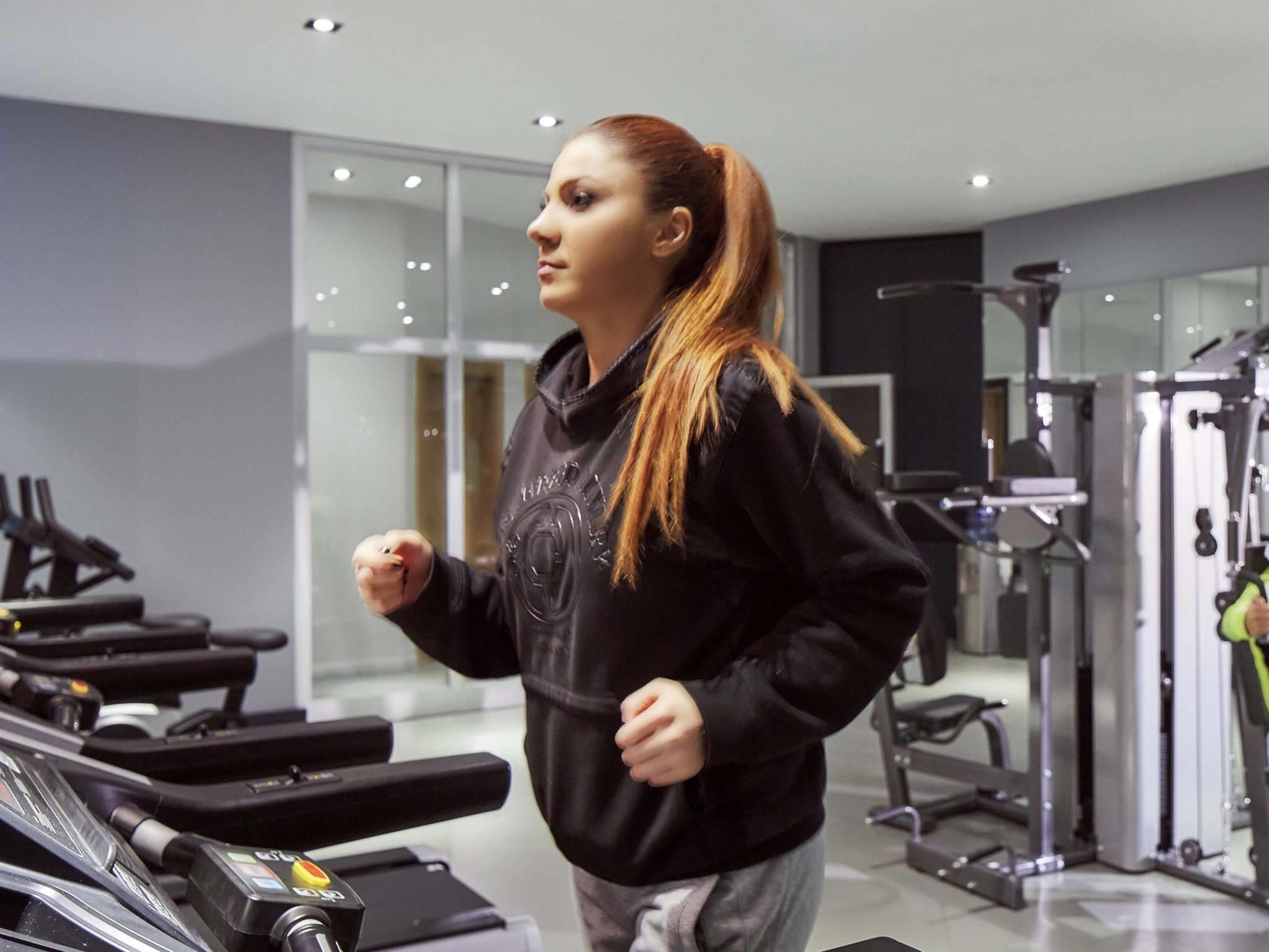 Un gimnasio con equipo de ejercicio, una cinta de correr y una persona con sudadera.