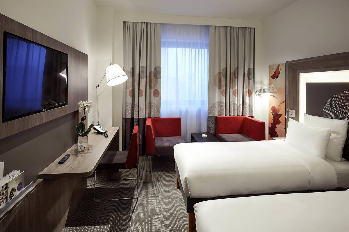 Una habitación de hotel con cama, escritorio con televisor, silla y una mesita.