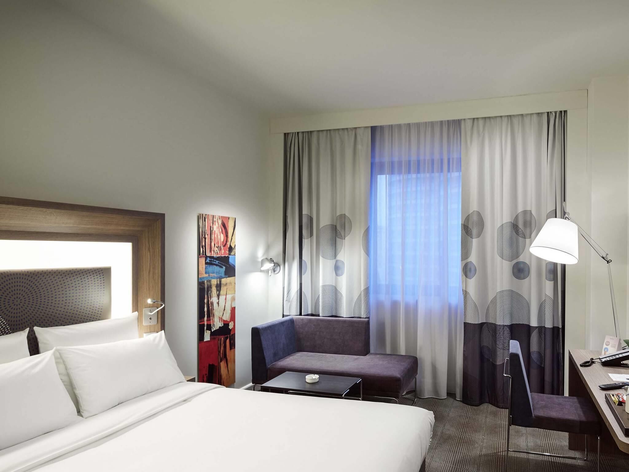 Ein Hotelzimmer mit einem Bett, einem Schreibtisch mit Stuhl, einer Couch, einer Lampe und einem Bild an der Wand.