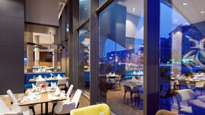 A modern restaurant with large windows offering a city view. - Novotel Konya (Konya)