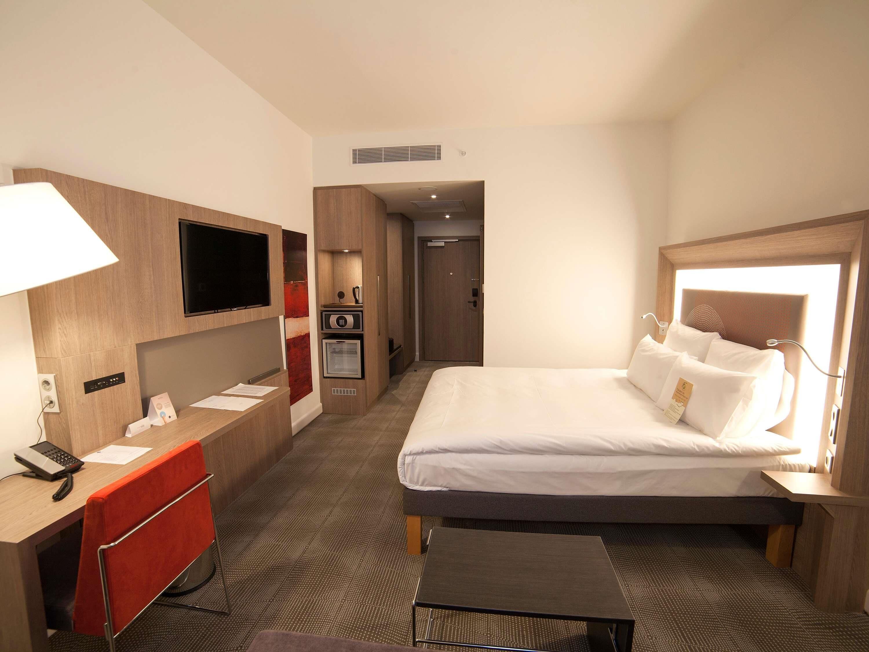 Quarto de hotel com cama, escrivaninha, telefone, televisão e minibar.
