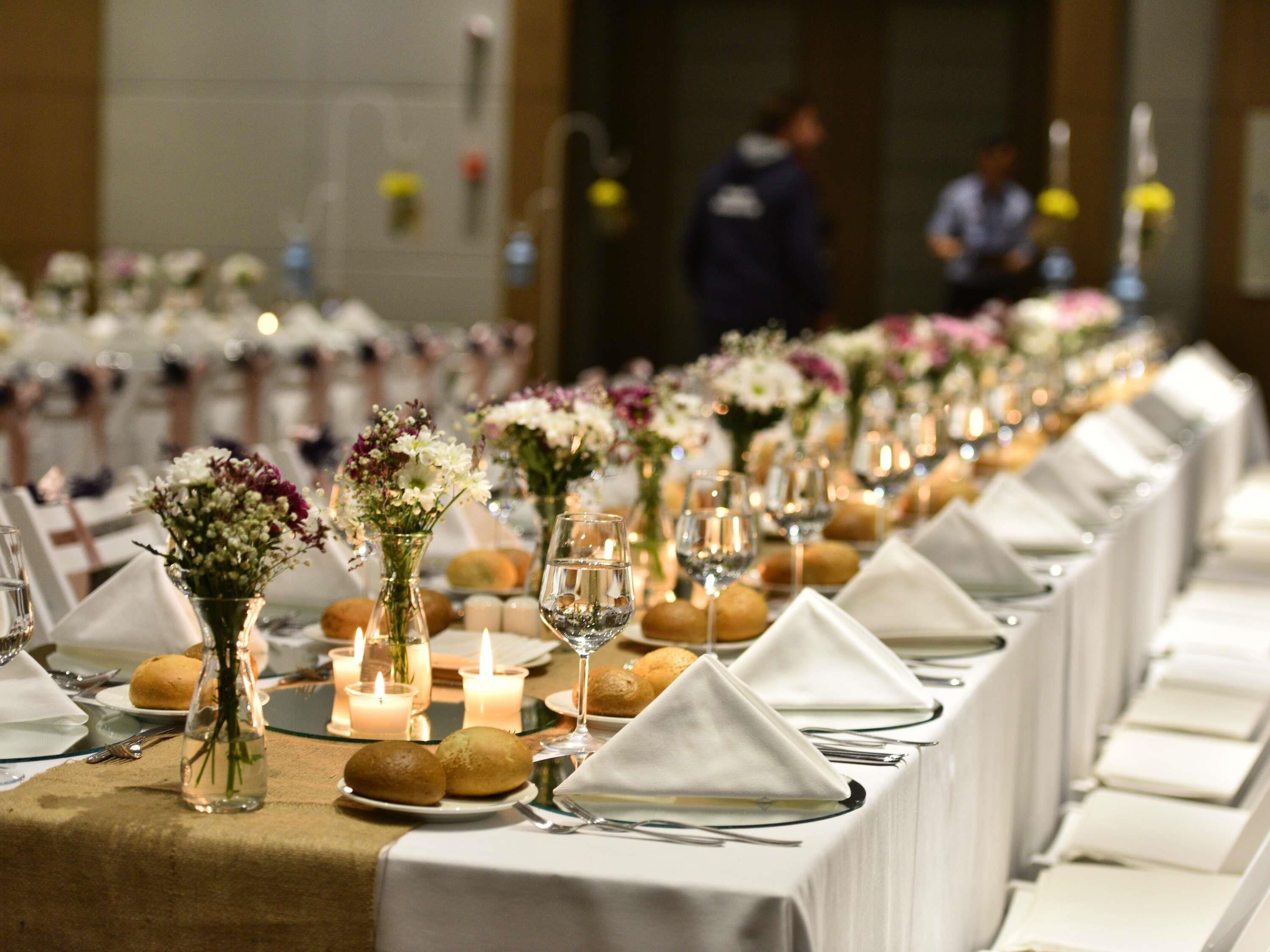 A long dining table with white tablecloths, set with plates, glasses, and candles, suggesting a formal dining setting.