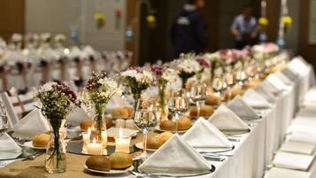 A long dining table with white tablecloths, set with plates, glasses, and candles, suggesting a formal dining setting.
