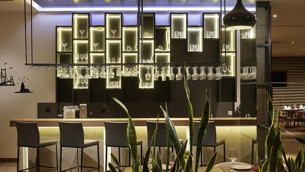 Un bar moderno con una barra larga, diversas opciones de asientos y una variedad de copas exhibidas en estanterías iluminadas.