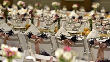 Un salón de banquetes con mesas redondas dispuestas para un evento formal, cada una con mantel blanco, cristalería y centros de mesa florales.