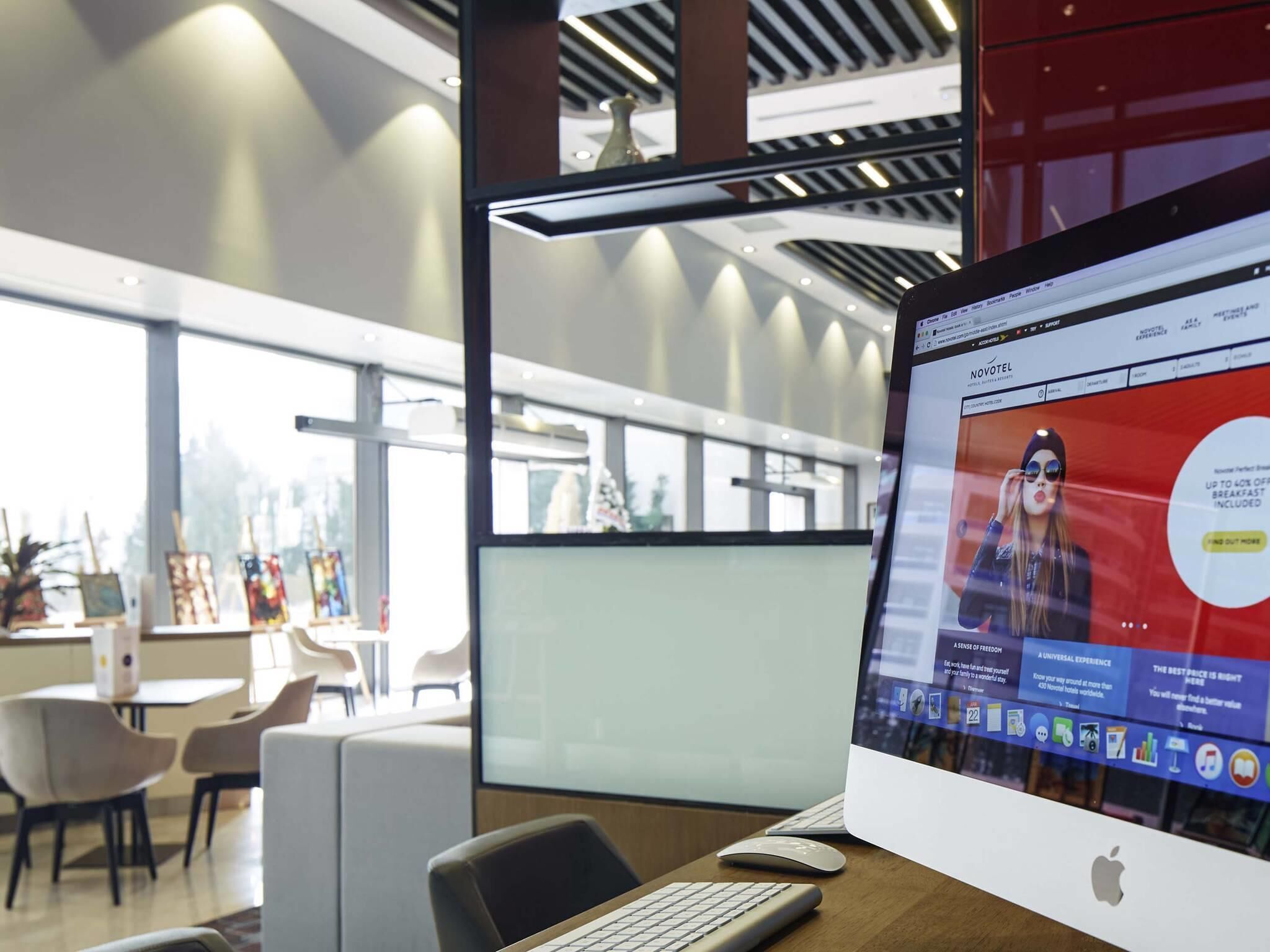 A modern office space with a laptop displaying a hotel website, a desk, chairs, and a view of the cityscape through large windows.