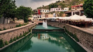 Un estrecho canal con una fuente, muros de piedra y edificios con terrazas al aire libre.