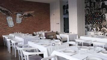 Un restaurante con mesas y sillas blancas, un mural de ladrillo y una pared de fotografías en blanco y negro.