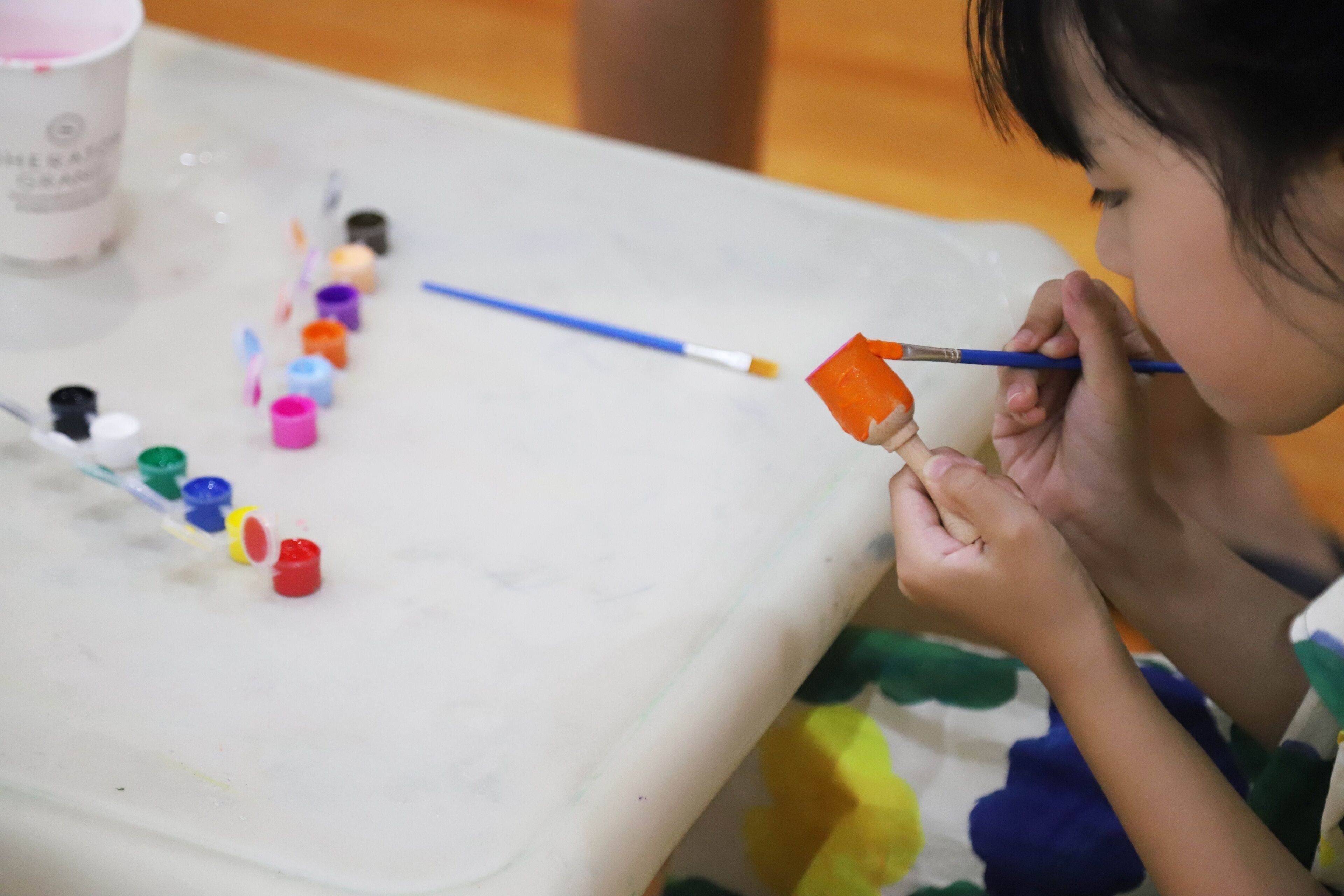 A child painting with a variety of small paint containers and a paintbrush on a table.