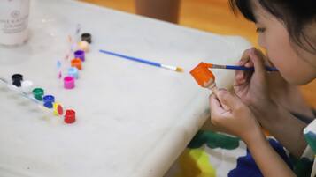 A child painting with a variety of small paint containers and a paintbrush on a table.