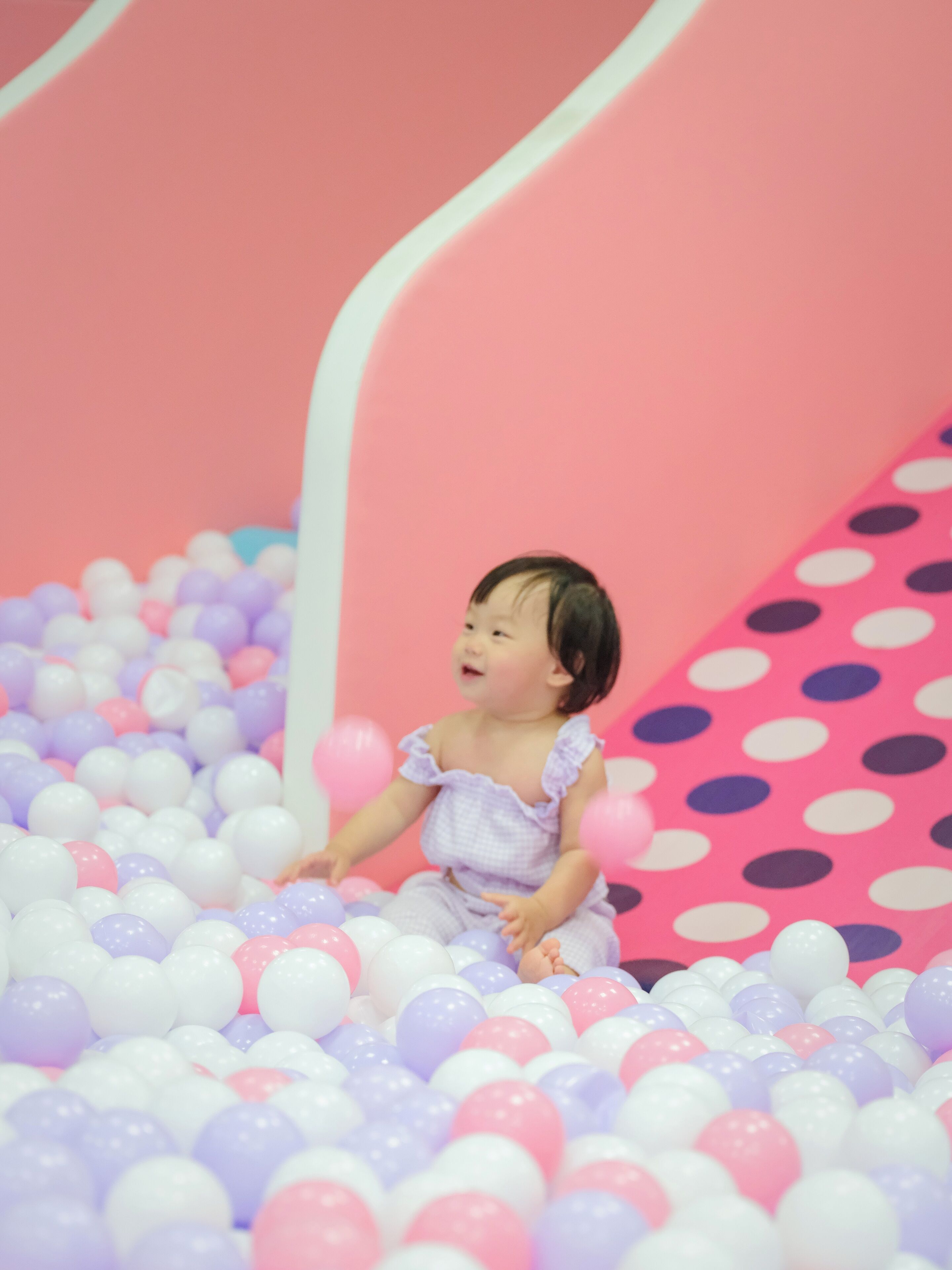 Un enfant dans une piscine à balles avec un toboggan rose.