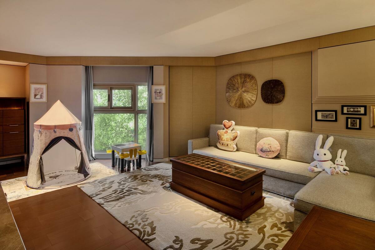 A cozy living room with a sofa, a wooden coffee table, a tent-like play area, and a dining table with chairs.