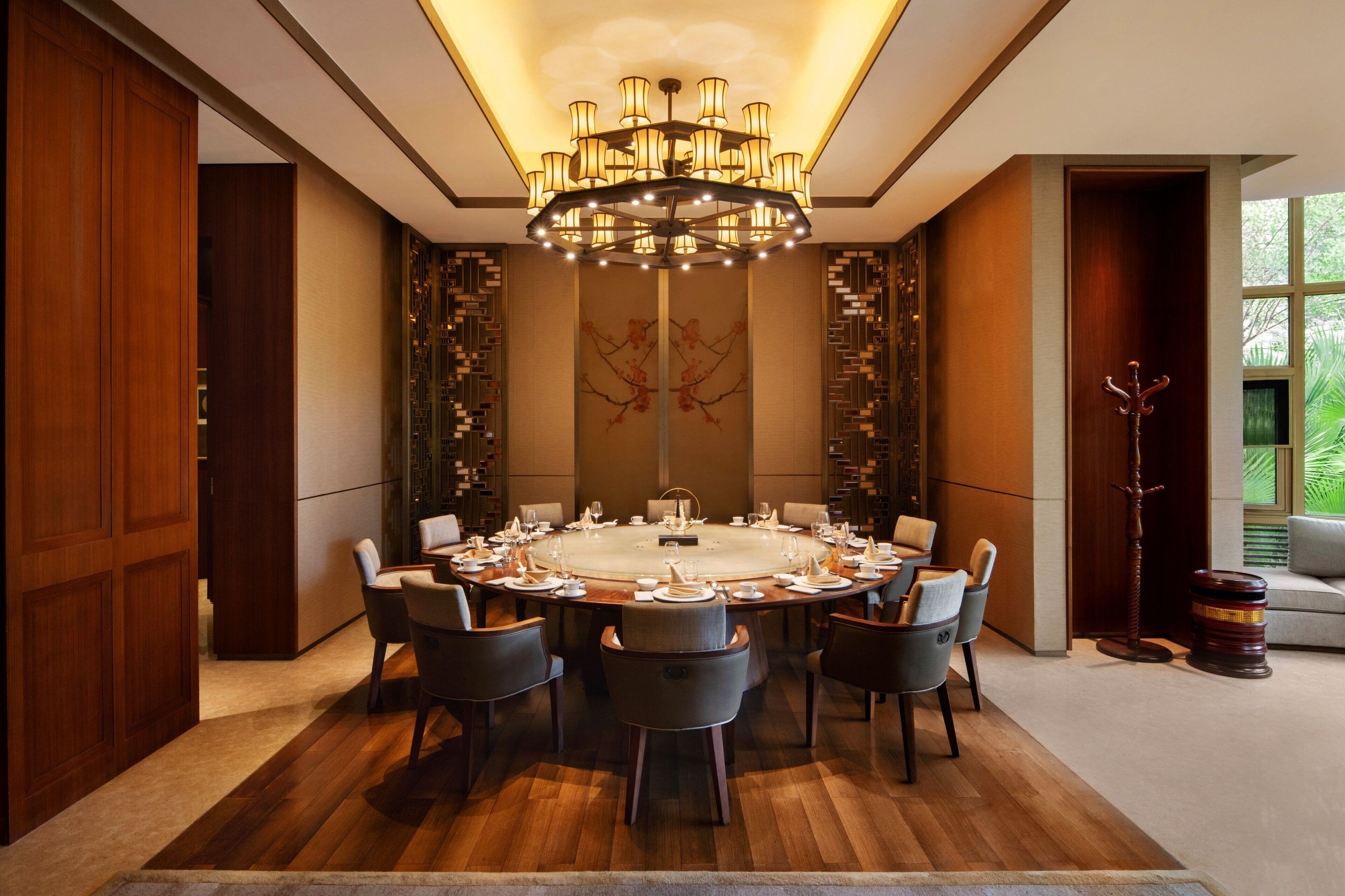 A round dining table with chairs, a chandelier, and a decorative wall piece.