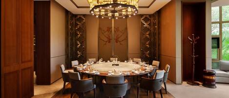 A round dining table with chairs, a chandelier, and a decorative wall piece.