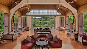 A spacious lounge area with a central seating arrangement, wooden ceiling, and large windows offering a view of greenery and a pool. - Sheraton Grand Xishuangbanna Hotel (Xishuangbanna Dai)
