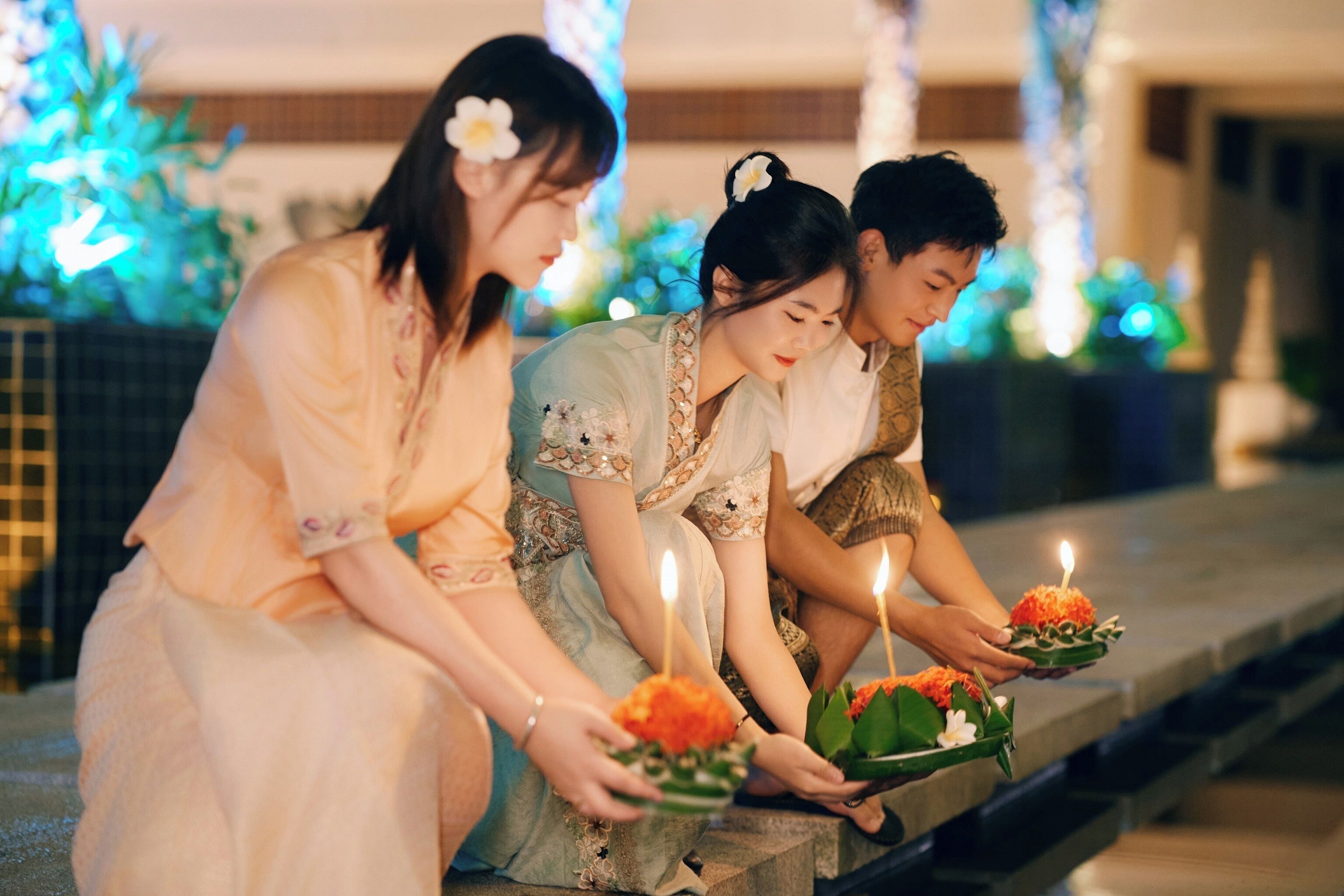Three people sitting on steps, each holding a candle with a lit flame.