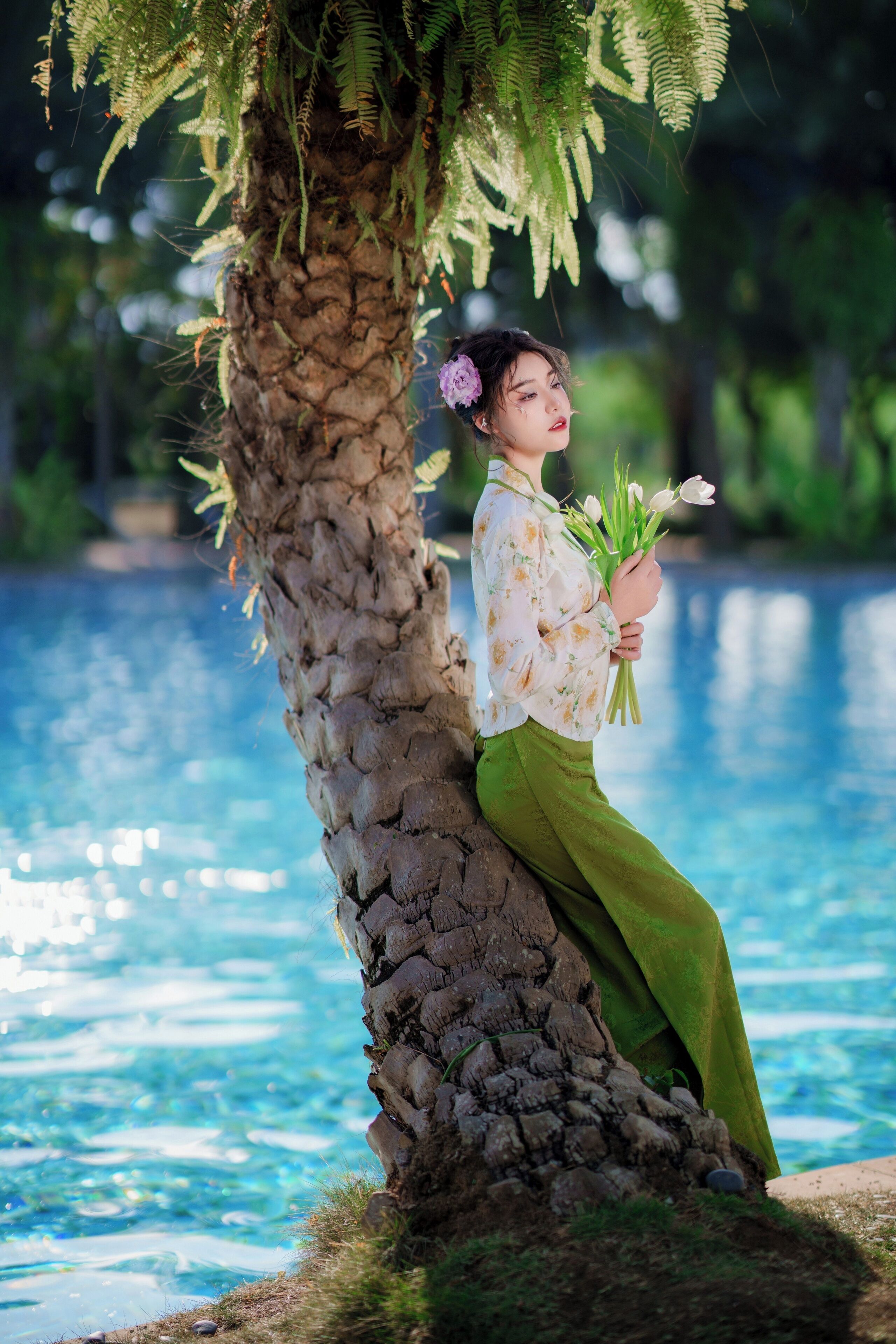 Una persona sentada junto a un árbol cerca de una piscina con agua.