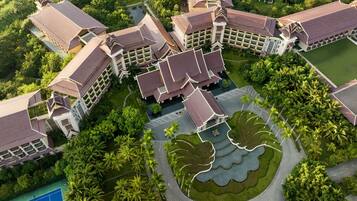 An aerial view of a resort with multiple buildings, a central courtyard with a water feature, and surrounding lush greenery.