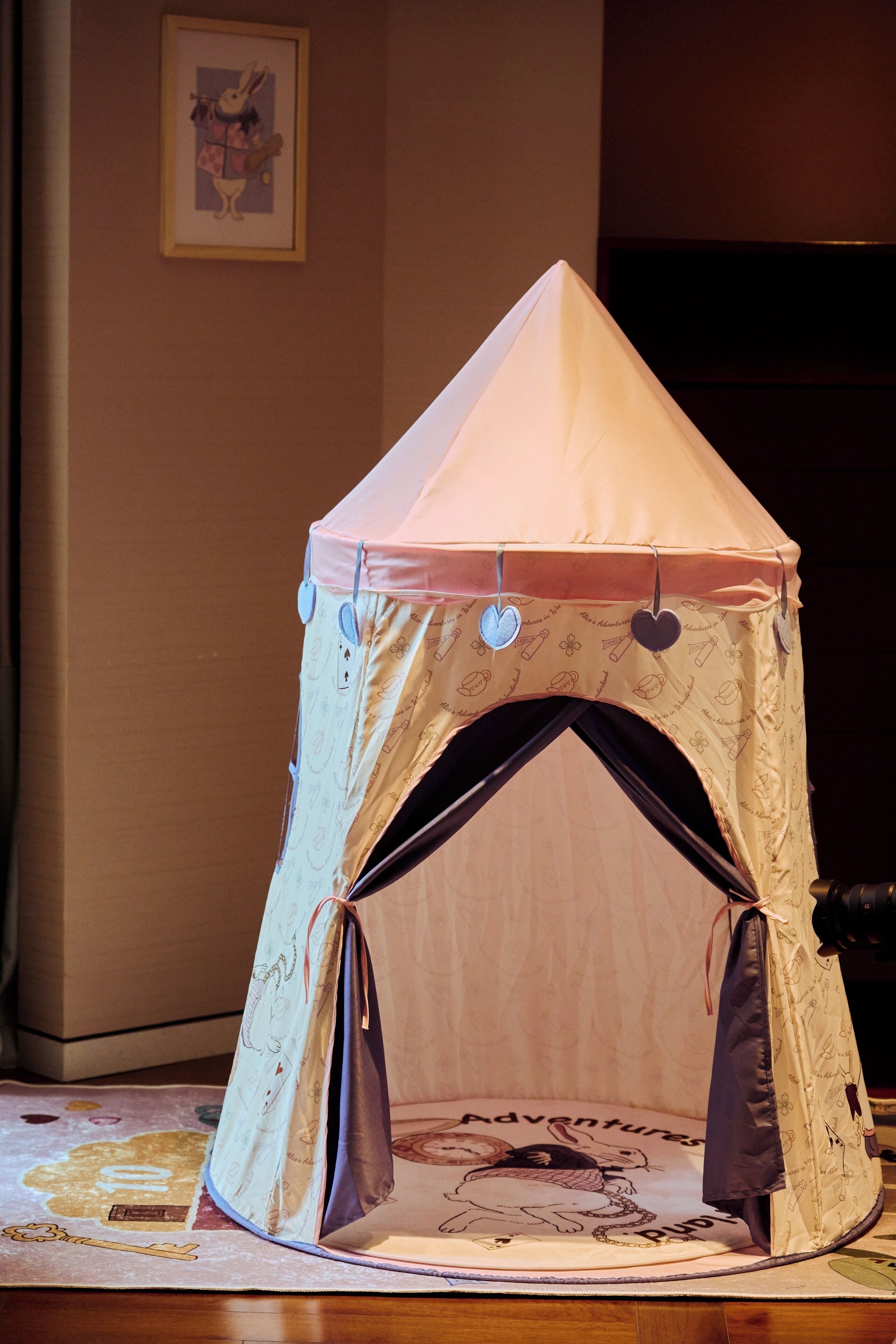 A small tent-like structure with a peaked roof and heart-shaped cutouts on the sides, placed on a patterned rug.