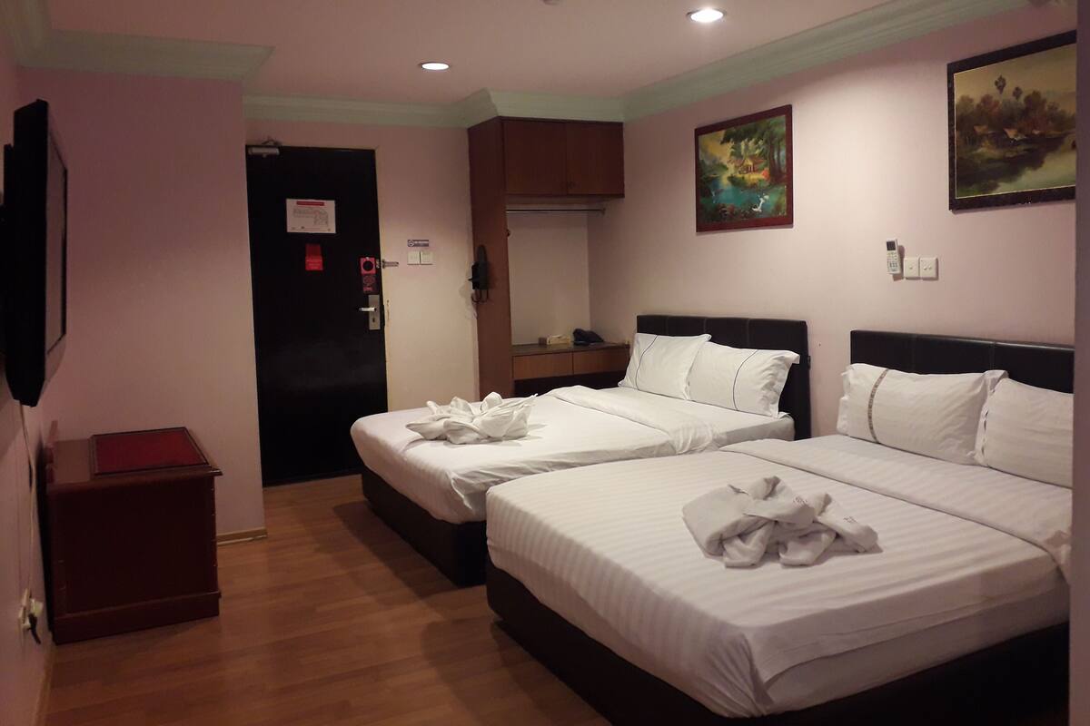 A hotel room with two beds, a wooden floor, a painting on the wall, and a small table with a red book.