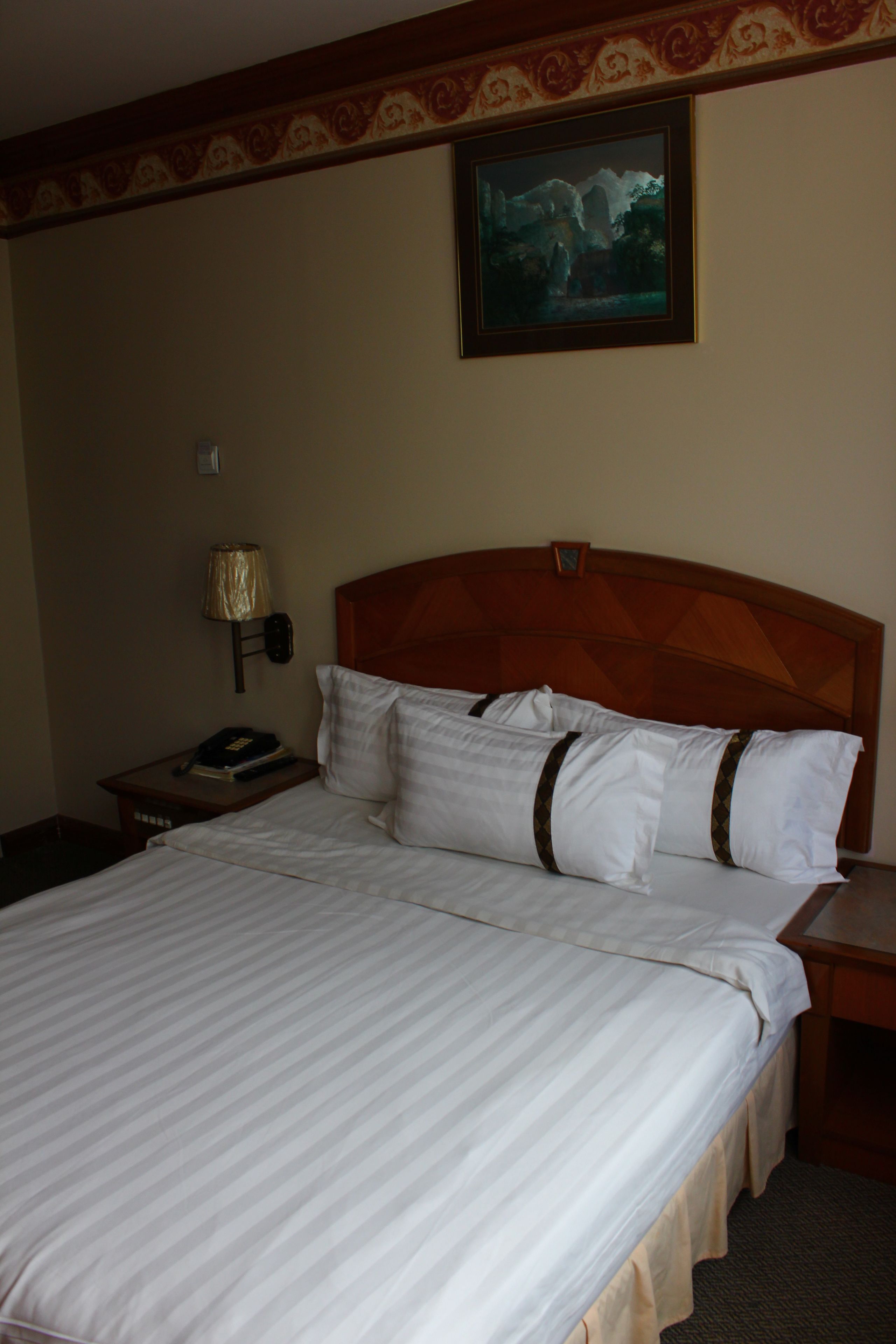 A hotel room with a large bed, a nightstand with a lamp, and a framed picture on the wall.