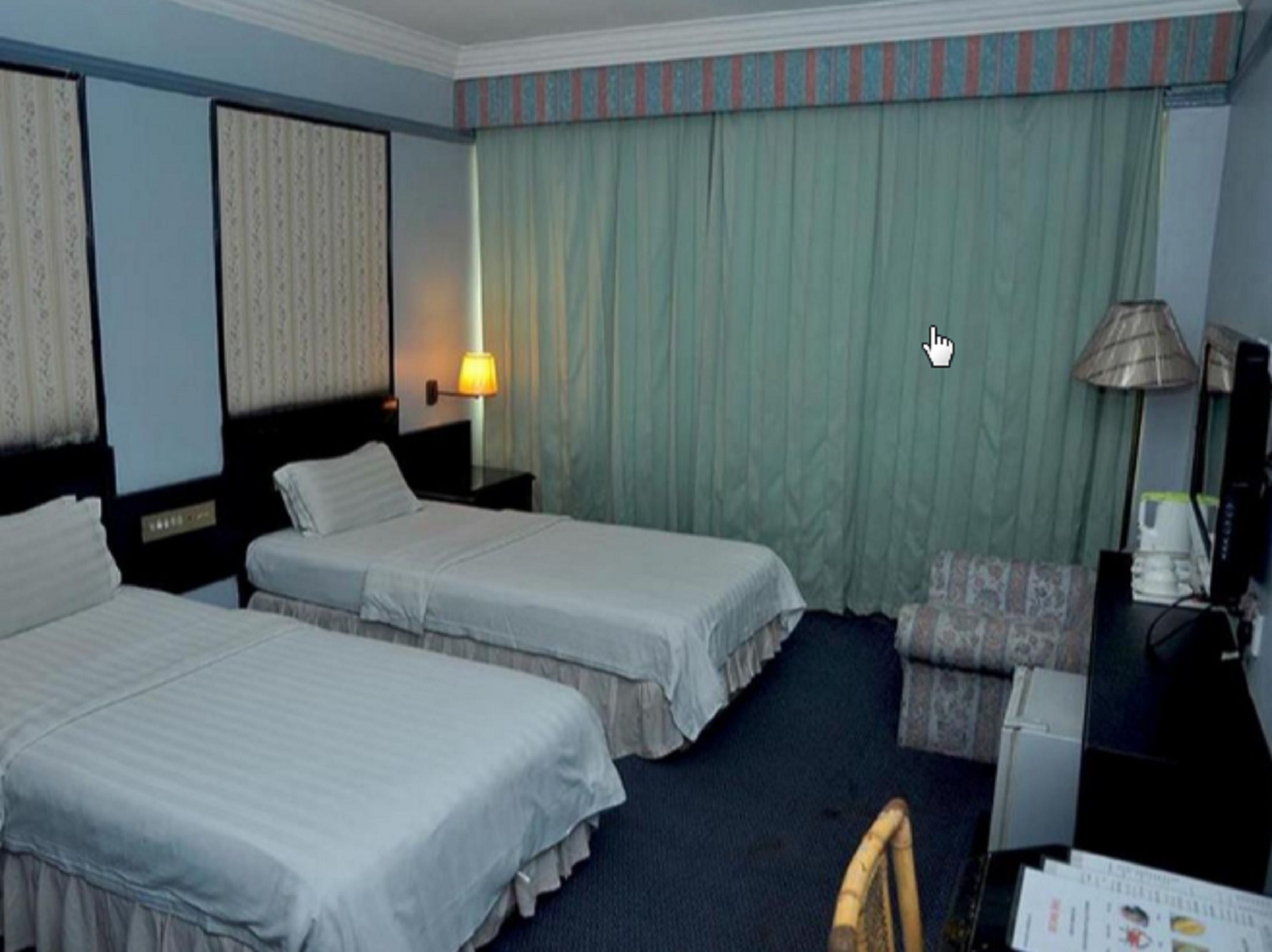 Quarto de hotel com duas camas, uma escrivaninha, uma cadeira, uma luminária e uma televisão.