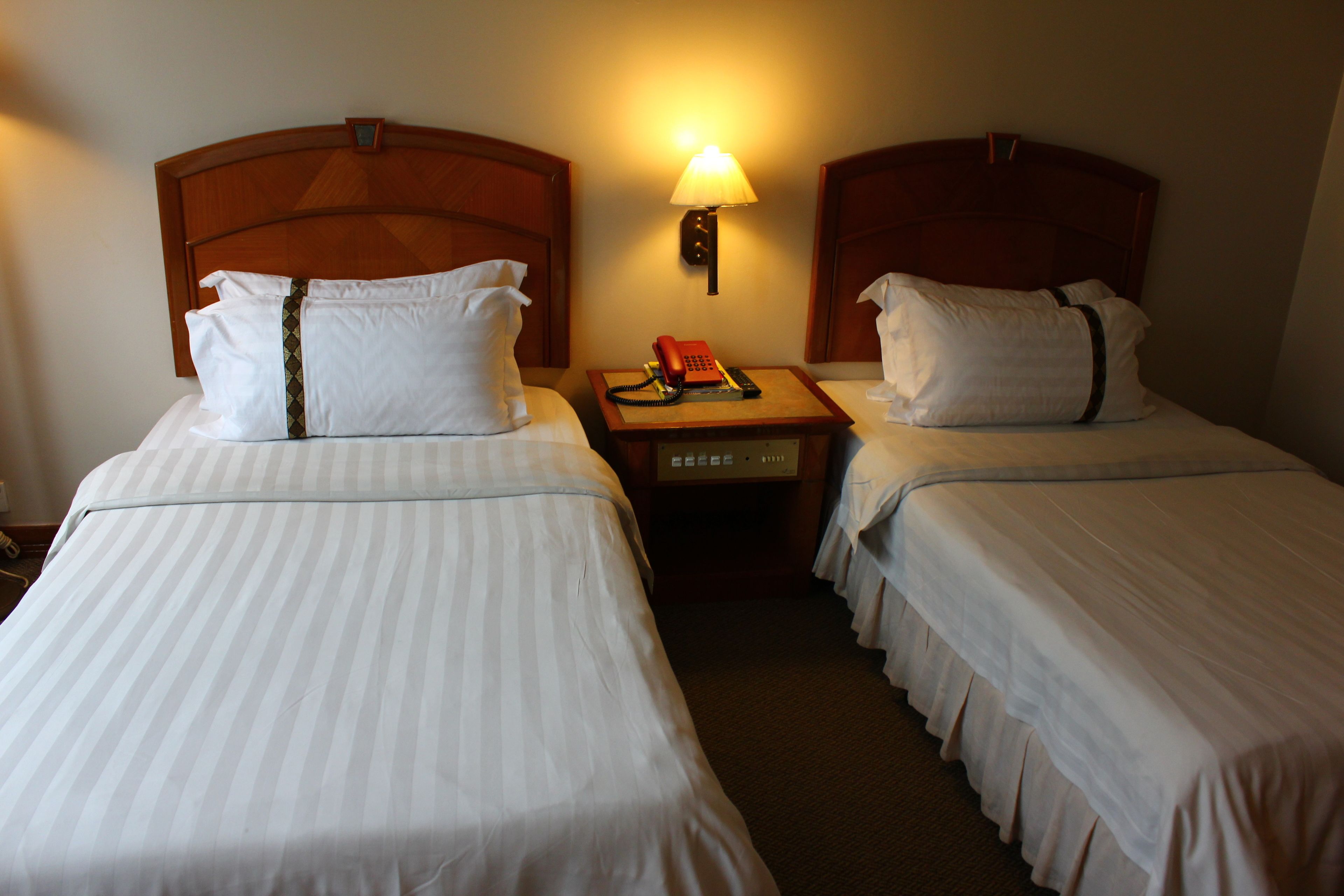 Una habitación de hotel con dos camas individuales, una mesita de noche con lámpara y un teléfono.