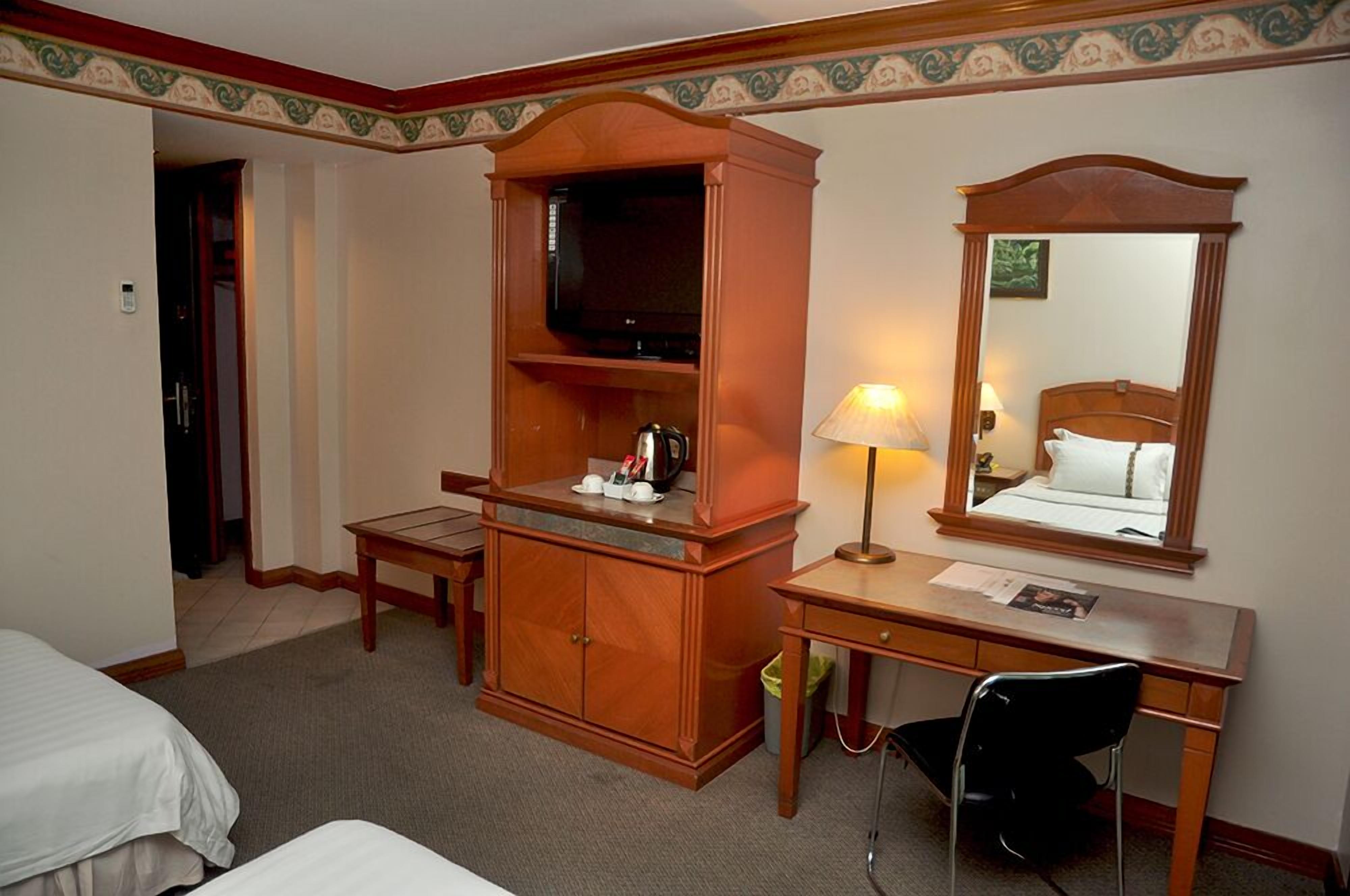 Habitación de hotel con un escritorio de madera, una silla, un televisor, una cama y un espejo.