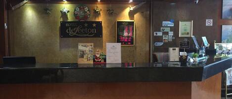 A hotel reception desk with a digital display, a 'Merry Christmas' sign, and various notices and cards on the wall.