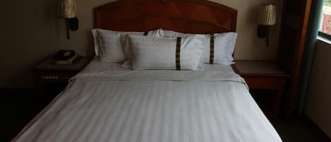 A neatly made bed with white linens and a wooden headboard, two bedside lamps, and a nightstand with a telephone and books.
